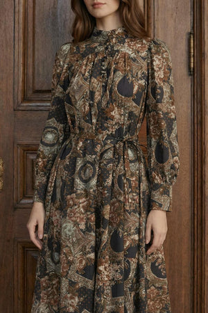 A close-up shows a long-sleeve vintage floral midi dress with a softly pleated bodice, tie waist detail, and muted earthy tones against a wooden backdrop.