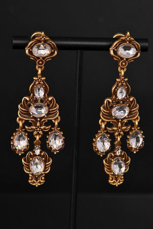 Close-up of antique gold chandelier earrings featuring faceted clear crystals set in ornate baroque-style frames.