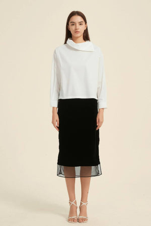 Model wearing a white asymmetric-collar blouse tucked into a black midi skirt with sheer layered hem — elegant contrast look from Sioéne.