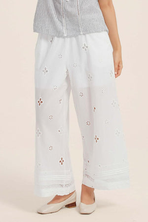 Front view of white wide-leg pants adorned with delicate floral eyelet embroidery and lace-edged hem, paired with a striped summer blouse.