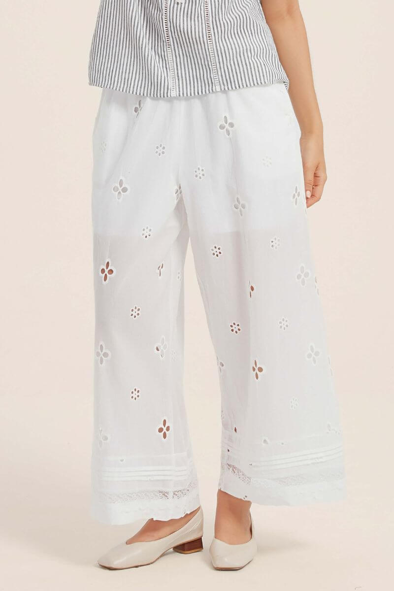 Front view of white wide-leg pants adorned with delicate floral eyelet embroidery and lace-edged hem, paired with a striped summer blouse.