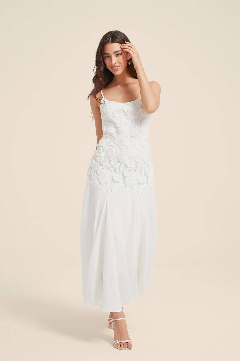 Front view of a white maxi dress with rosette floral appliqués and flowy chiffon skirt, featuring slim straps and a soft romantic silhouette.