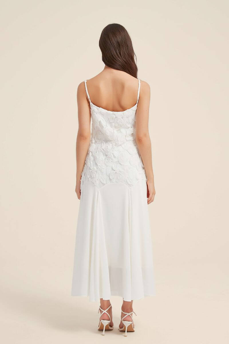 Back view of a white floral lace maxi dress with spaghetti straps and textured appliqué bodice, showing the elegant low-back design and flowy skirt.