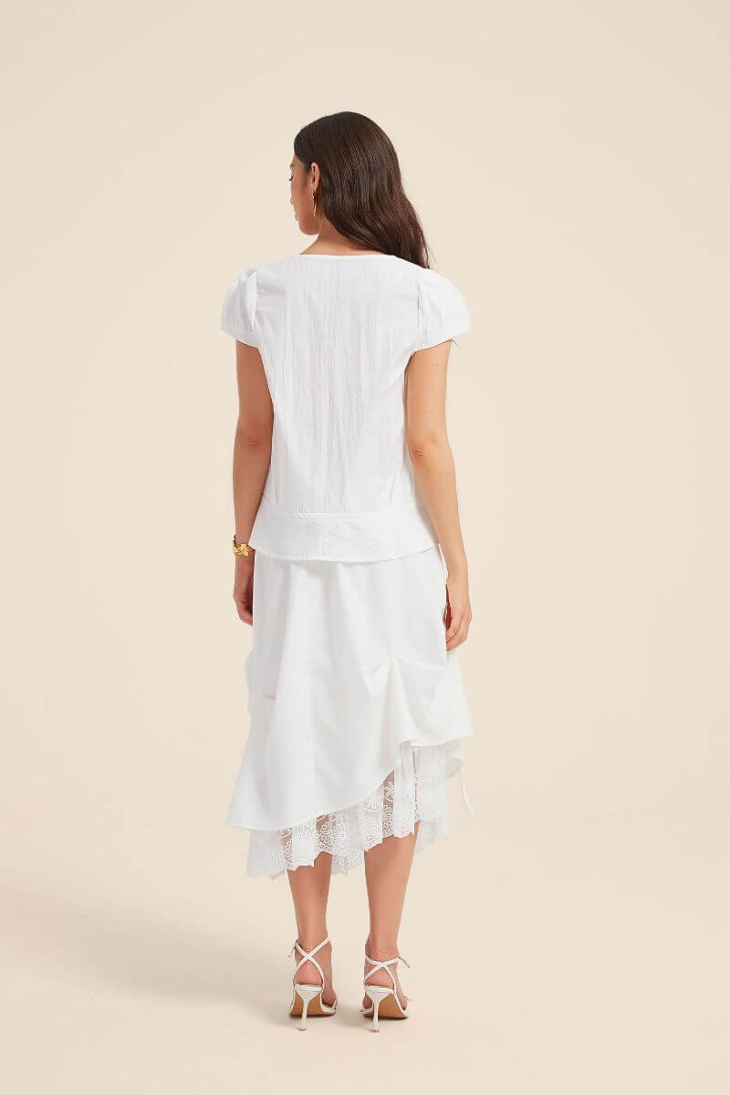 Back view of a woman wearing a white lace-trim blouse and bow-draped skirt set, highlighting the tiered structure and lace-edged hemline.