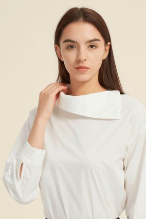 Close-up of a white long-sleeve blouse with a sculptural asymmetric collar and buttoned cuffs — a clean, modern silhouette from Sioéne.