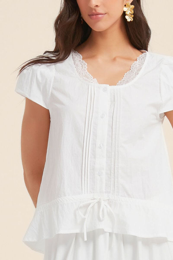 Close-up of a white pintuck blouse with lace-trim neckline and tie hem, featuring delicate cotton texture and romantic feminine detailing.