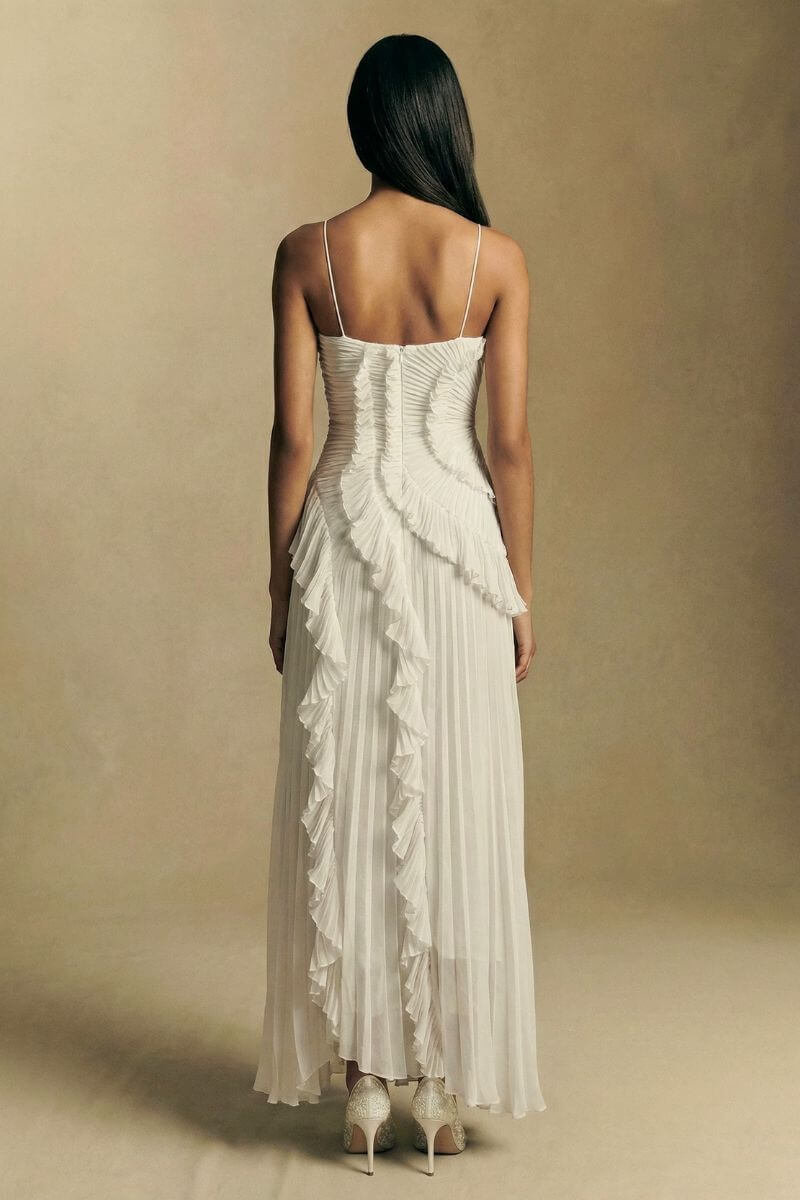 Back view of a white pleated halter midi dress featuring slim straps, a softly ruched back bodice, and cascading ruffle details down the skirt.