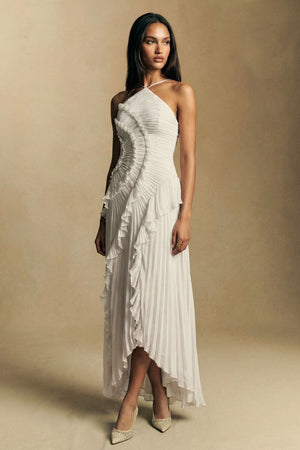 Model poses in profile wearing a white pleated halter midi dress with flowing ruffles that create a soft, sculpted side silhouette.