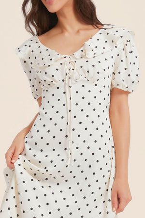 Close-up of a white polka dot midi dress showing the delicate ruffled neckline, drawstring tie, and soft satin texture of the lightweight fabric.