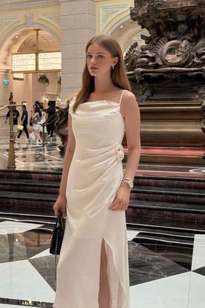 Woman wearing a white satin midi dress with floral appliqué, photographed indoors under warm lights in an elegant architectural hall.