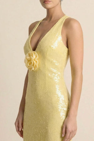 Close-up view of a woman wearing a yellow sequin deep-V evening gown featuring a soft floral appliqué at the bust, shown against a neutral studio background.
