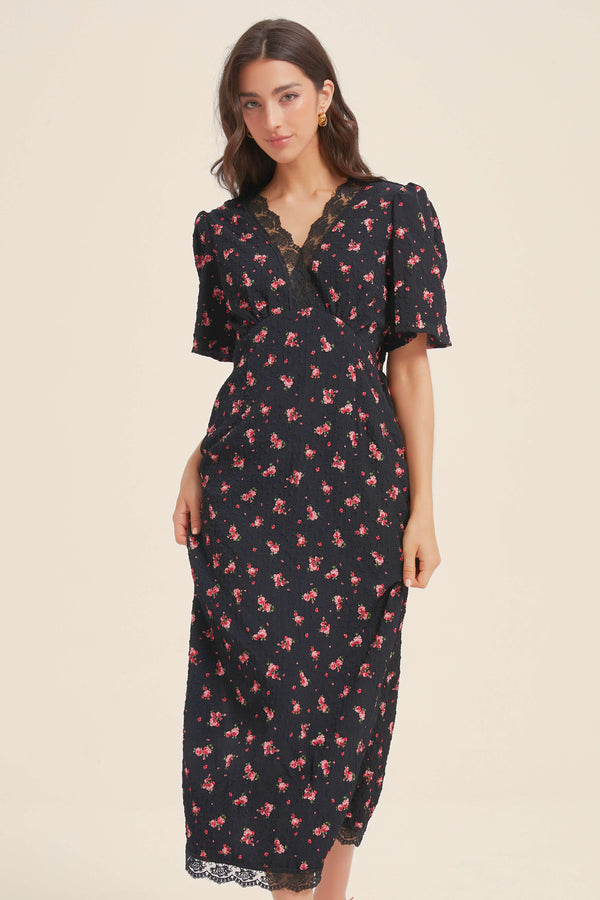 Front view of a woman wearing a black midi dress with red floral print, V-neckline, puff sleeves, and delicate lace trim at the neckline and hem.