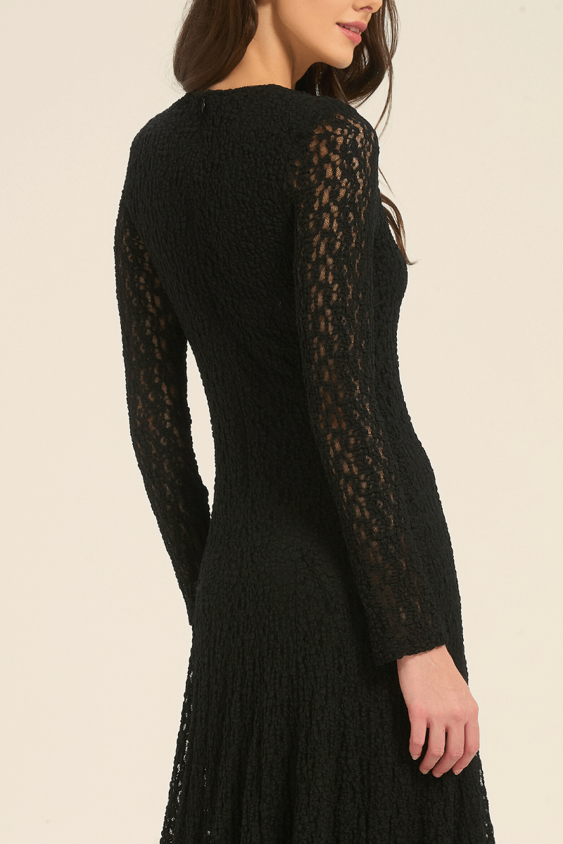 Side view of black lace long sleeve maxi dress featuring semi-sheer sleeves and a fitted waist.