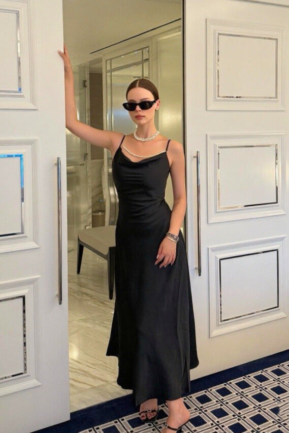 Woman in a black satin maxi dress styled with pearl necklace and sunglasses for an elegant evening look