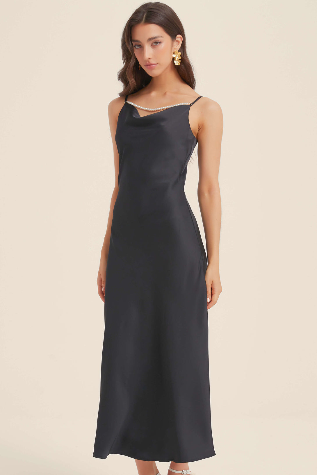 Woman wearing black satin maxi dress with pearl-trim neckline and spaghetti straps, front view.