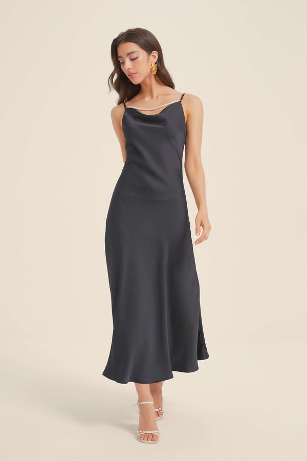Woman wearing a black satin slip dress with pearl strap detailing and a flowing hemline.