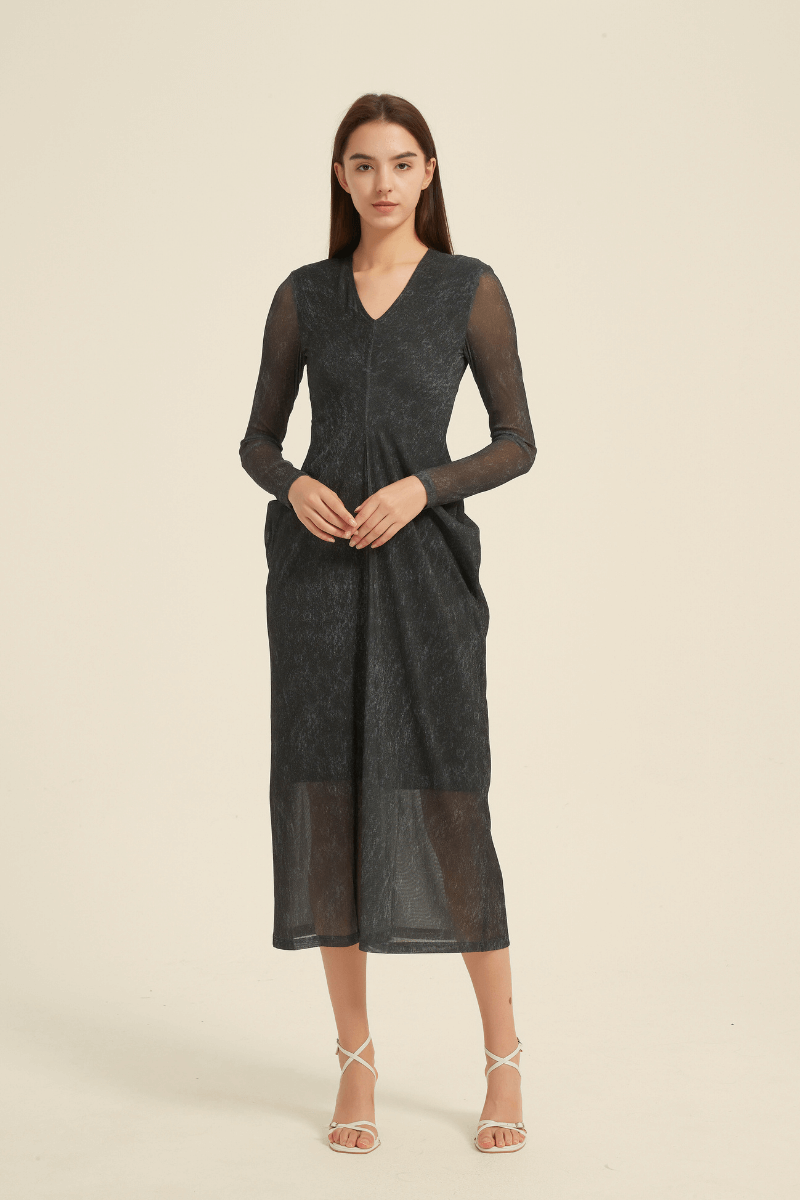 Model wearing a black sheer long sleeve midi dress with V-neckline, fitted bodice, and flowy hem, styled with strappy heels.