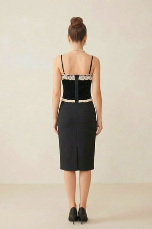 Back view of a model wearing a black velvet corset with cream lace trim paired with a black pencil skirt against a neutral studio background.