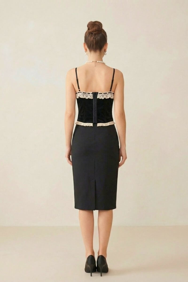Back view of a model wearing a black velvet corset with cream lace trim paired with a black pencil skirt against a neutral studio background.