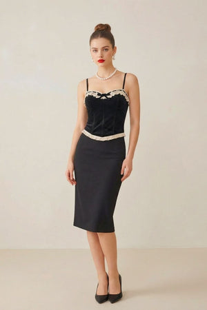 Full-body view of a model in a black velvet lace-trim corset paired with a black pencil skirt and classic heels in a neutral-toned studio.