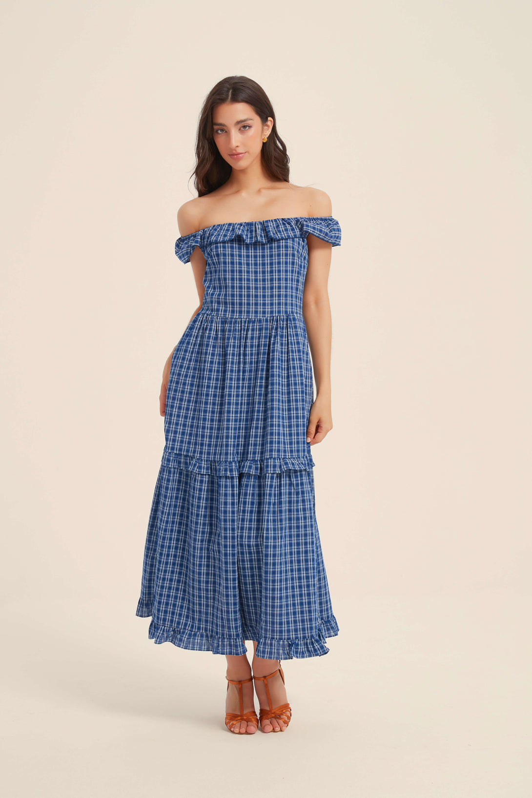 Woman wearing a blue off-shoulder gingham maxi dress with ruffle trim, perfect for summer getaways or outdoor brunches.