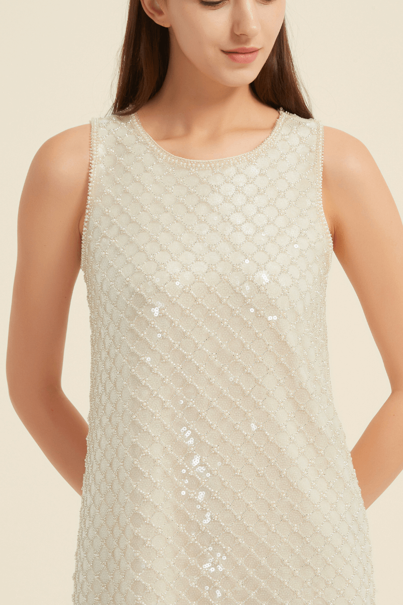 Close-up view of a champagne mini dress featuring an intricate diamond-patterned sequin design with delicate beaded edges and a round neckline, highlighting the shimmer and texture of the fabric.