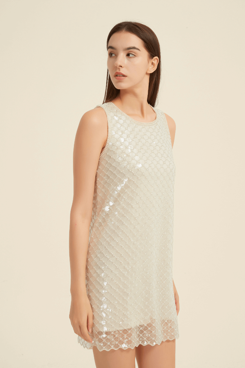 Side view of a champagne mini dress adorned with a diamond-patterned sequin overlay and scalloped hem, featuring a sleeveless cut and round neckline for a sleek, elegant look.