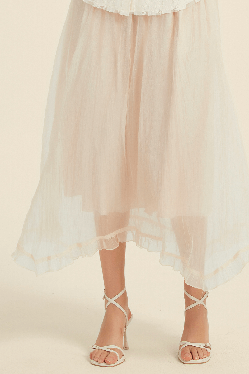 Close-up view of an ivory midi skirt featuring sheer layered fabric with a subtle ruffled hem, paired with white strappy sandal.
