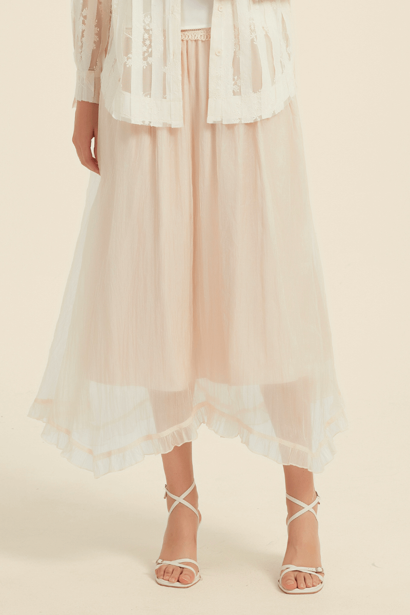 Close-up view of an ivory midi skirt featuring sheer layered fabric with a subtle ruffled hem, paired with white strappy sandal.