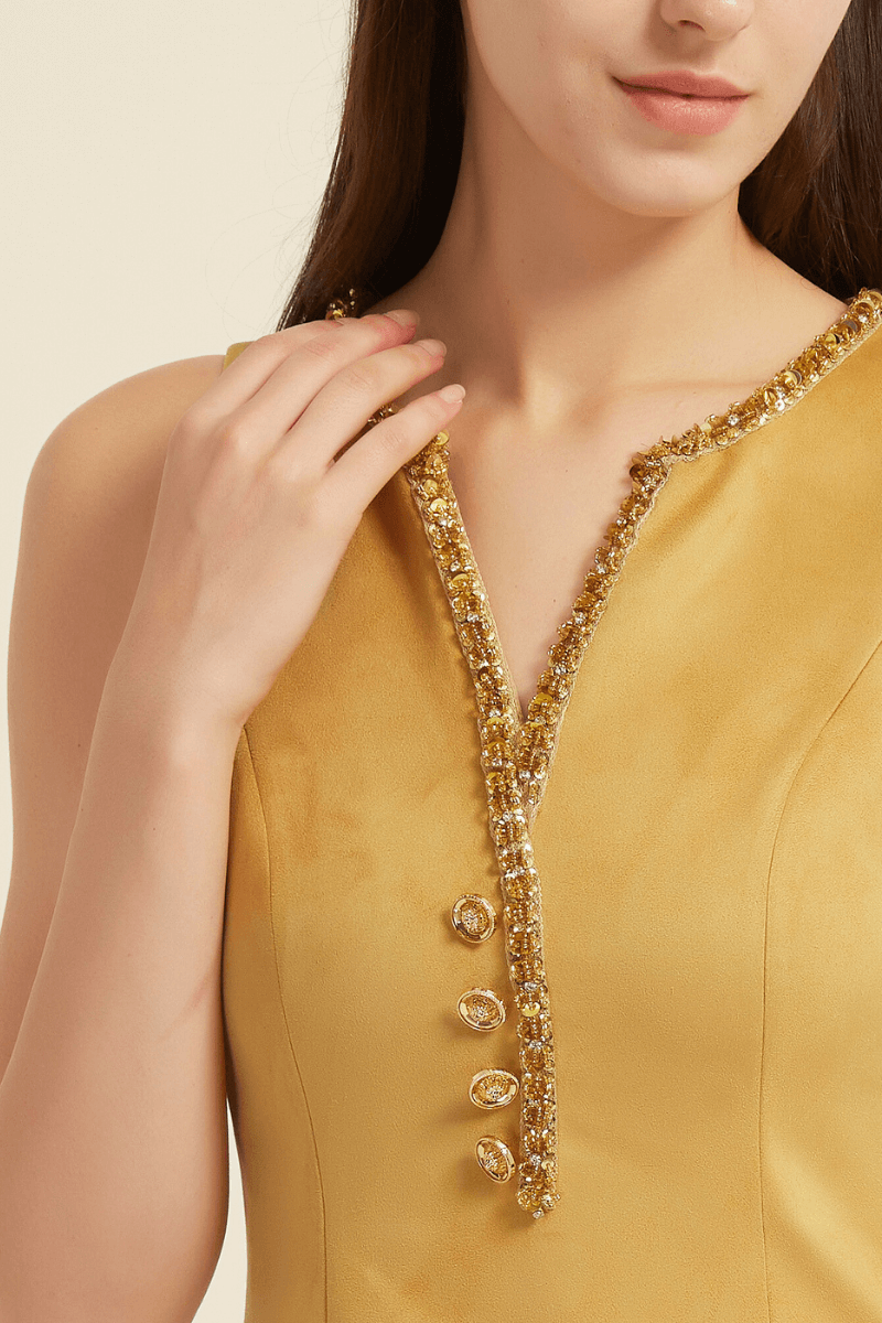 Close-up view of a yellow sleeveless mini dress featuring a beaded V-neckline, decorative gemstone buttons, and pocket trims with matching beadwork.