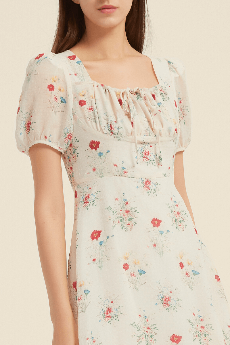 Close-up of a cream midi dress featuring a delicate floral print, square neckline, puff sleeves, and a tie-front detail, highlighting the fitted bodice and vintage-inspired design.