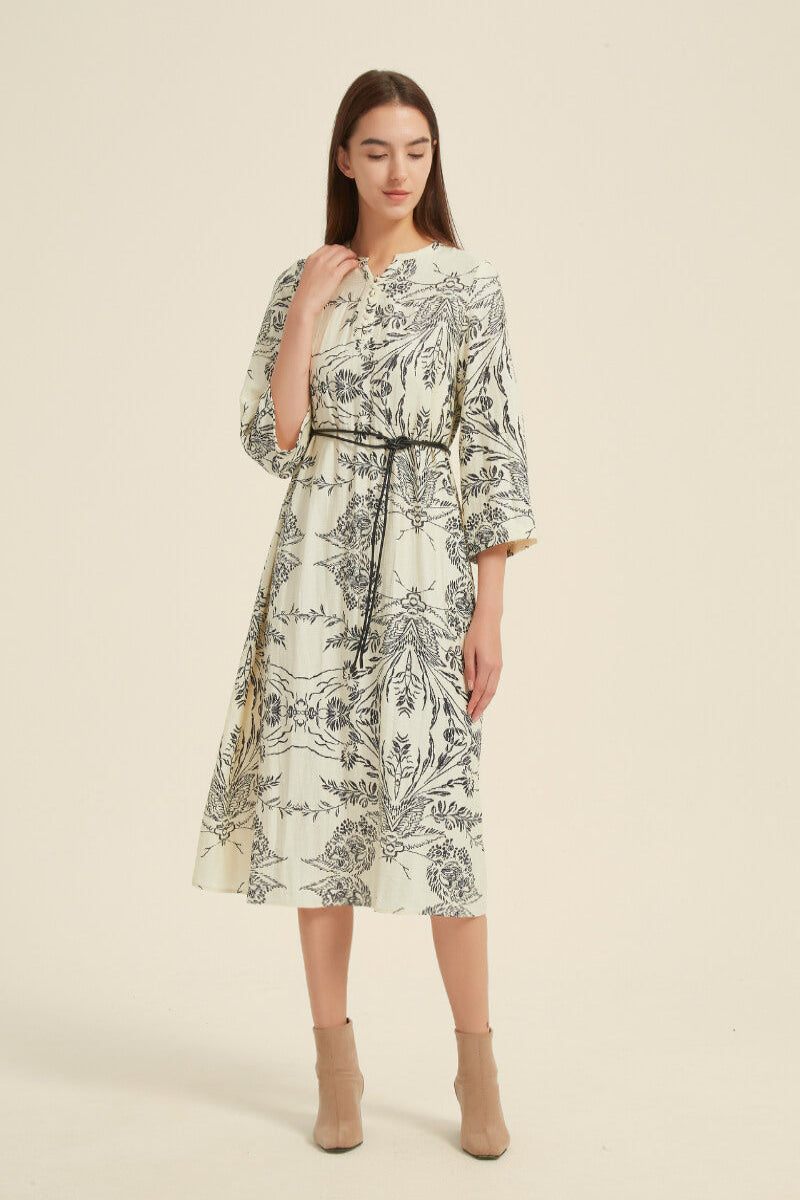 Woman wearing a cream midi dress with black floral print, featuring 3/4 sleeves, a belted waist tie, and flowy A-line silhouette.