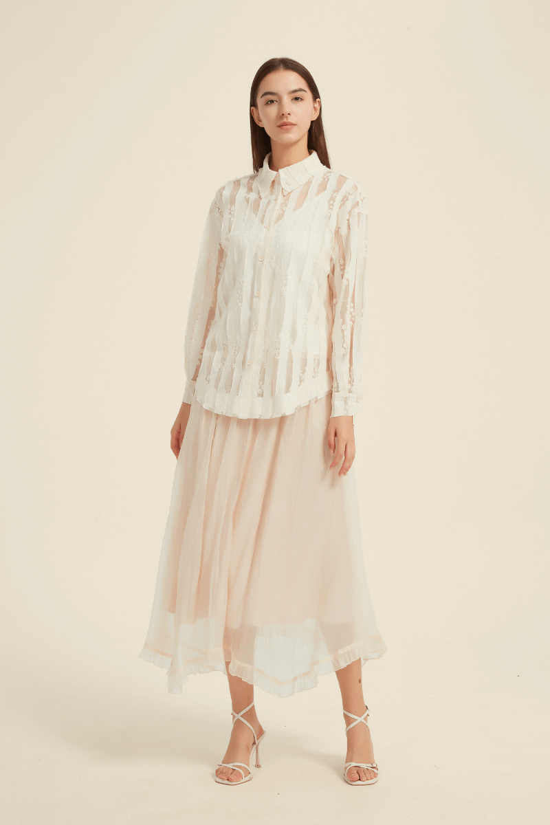 Front view of a model wearing an ivory sheer stripe blouse with a collared neckline and long sleeves, paired with a flowy ivory midi skirt featuring a ruffled hem.