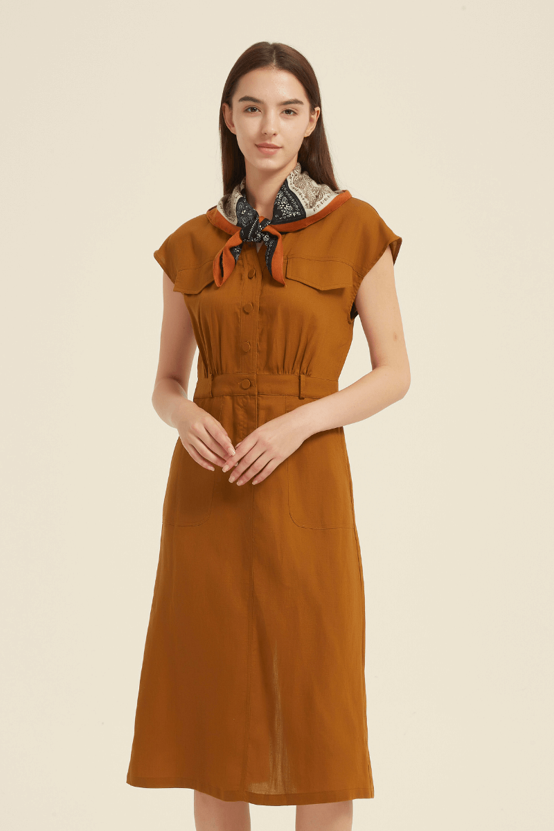 Front view of a rust cap sleeve midi shirt dress with a button-down front, elastic waist, front patch pockets, and a printed scarf tied at the neck.