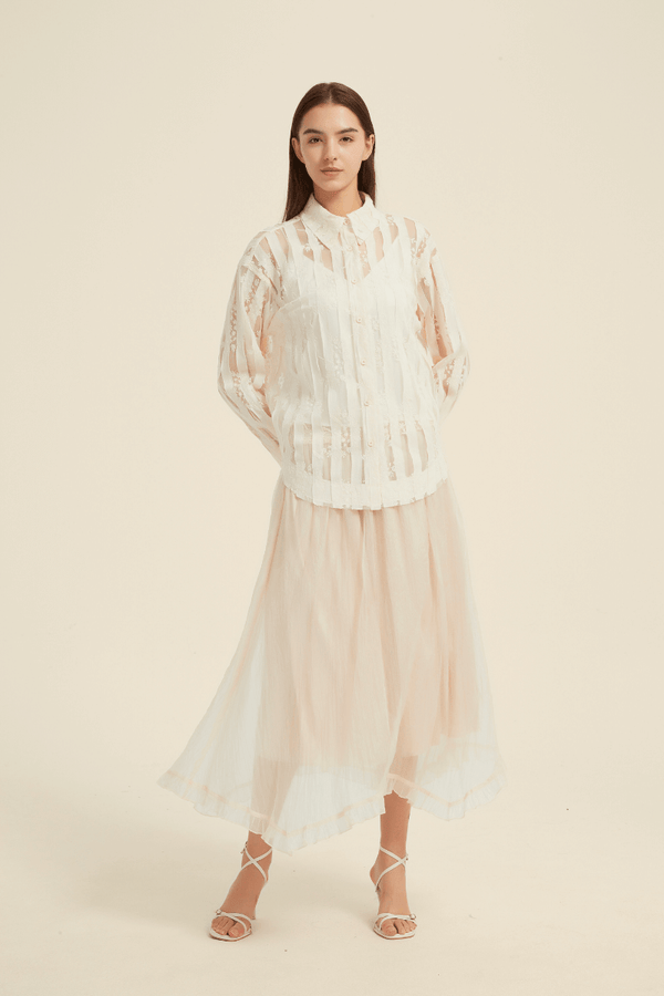 Front view of a model wearing a sheer lace striped blouse with a collared neckline and long sleeves, paired with a flowing ivory midi skirt and strappy sandals.
