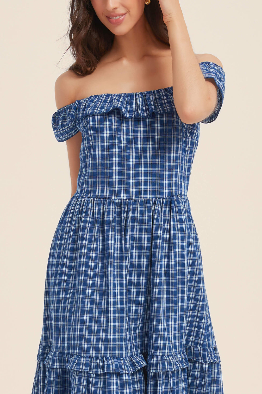Close-up of a woman wearing a blue gingham off-shoulder maxi dress with ruffle neckline and tiered skirt — breezy and charming for warm days.