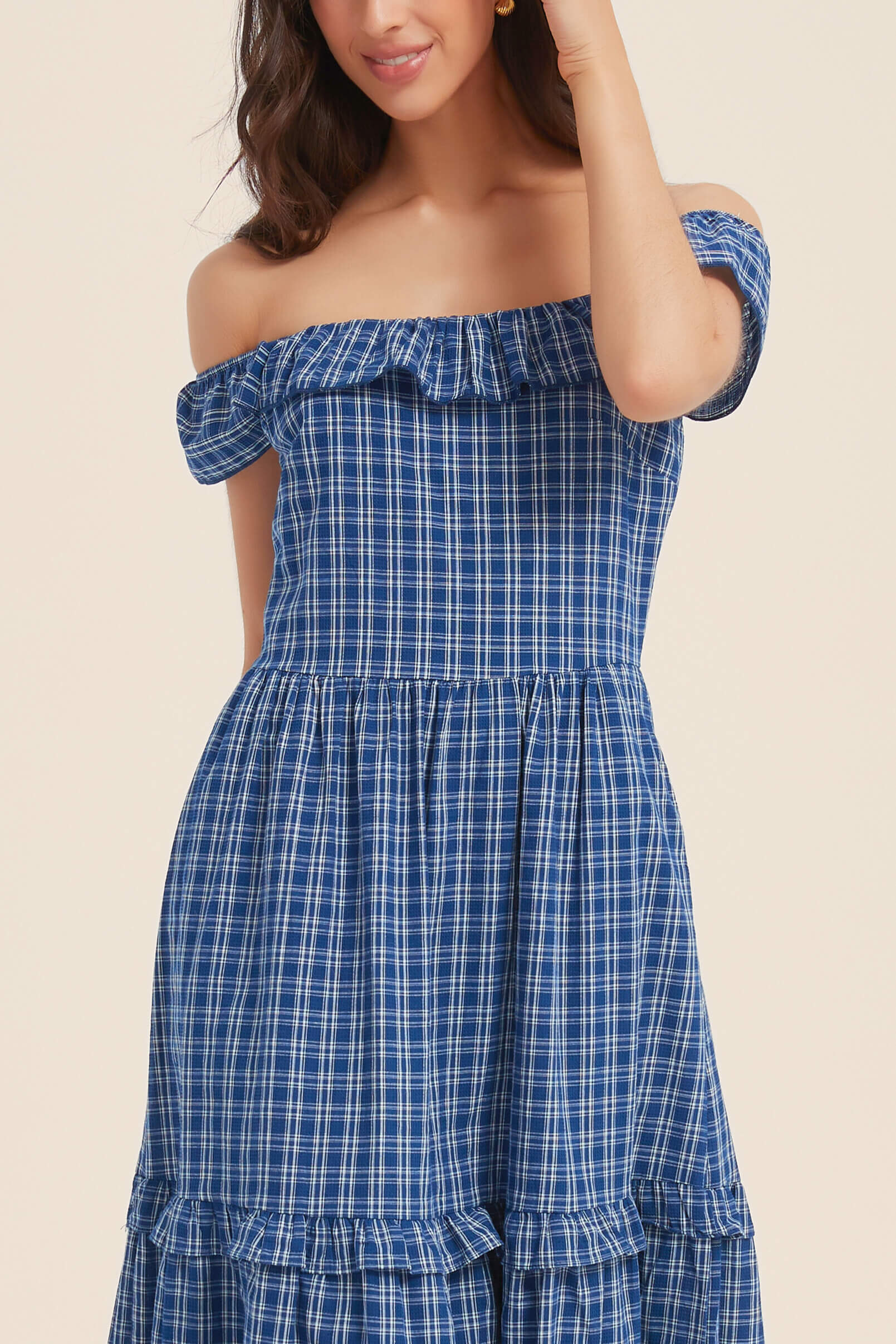 Close-up of a woman wearing a blue gingham off-shoulder maxi dress with ruffle neckline and tiered skirt — breezy and charming for warm days.