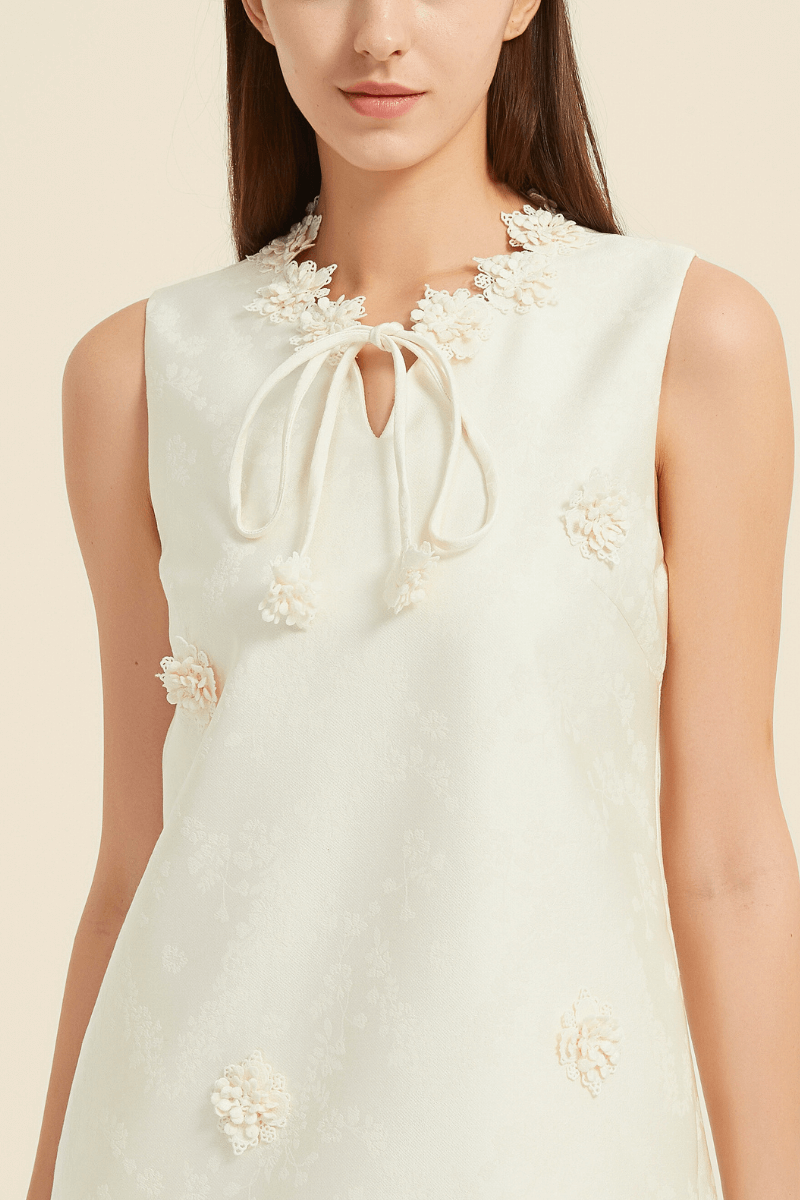 Detailed view of ivory mini dress featuring floral lace appliqués around the neckline and a delicate tie at the keyhole front.