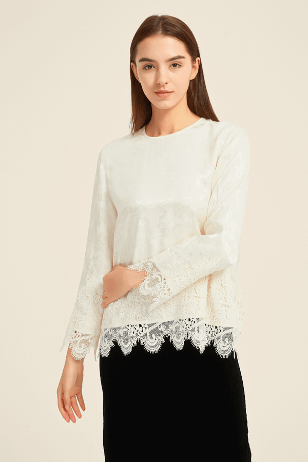 Woman wearing an ivory long-sleeve blouse with floral lace trim on cuffs and hem, styled with a black skirt, elegant and feminine design.