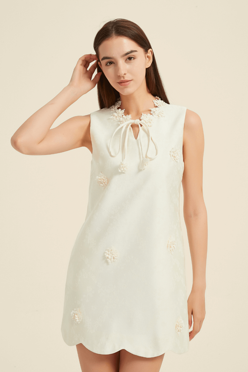 Close-up of ivory mini dress with floral appliqués, scalloped hem, and a keyhole tie-neckline, highlighting the delicate embroidery details.
