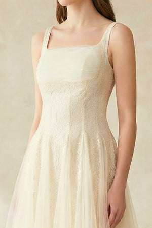 A close-up of the bodice of an ivory lace tulle dress showing textured lace details and wide straps.