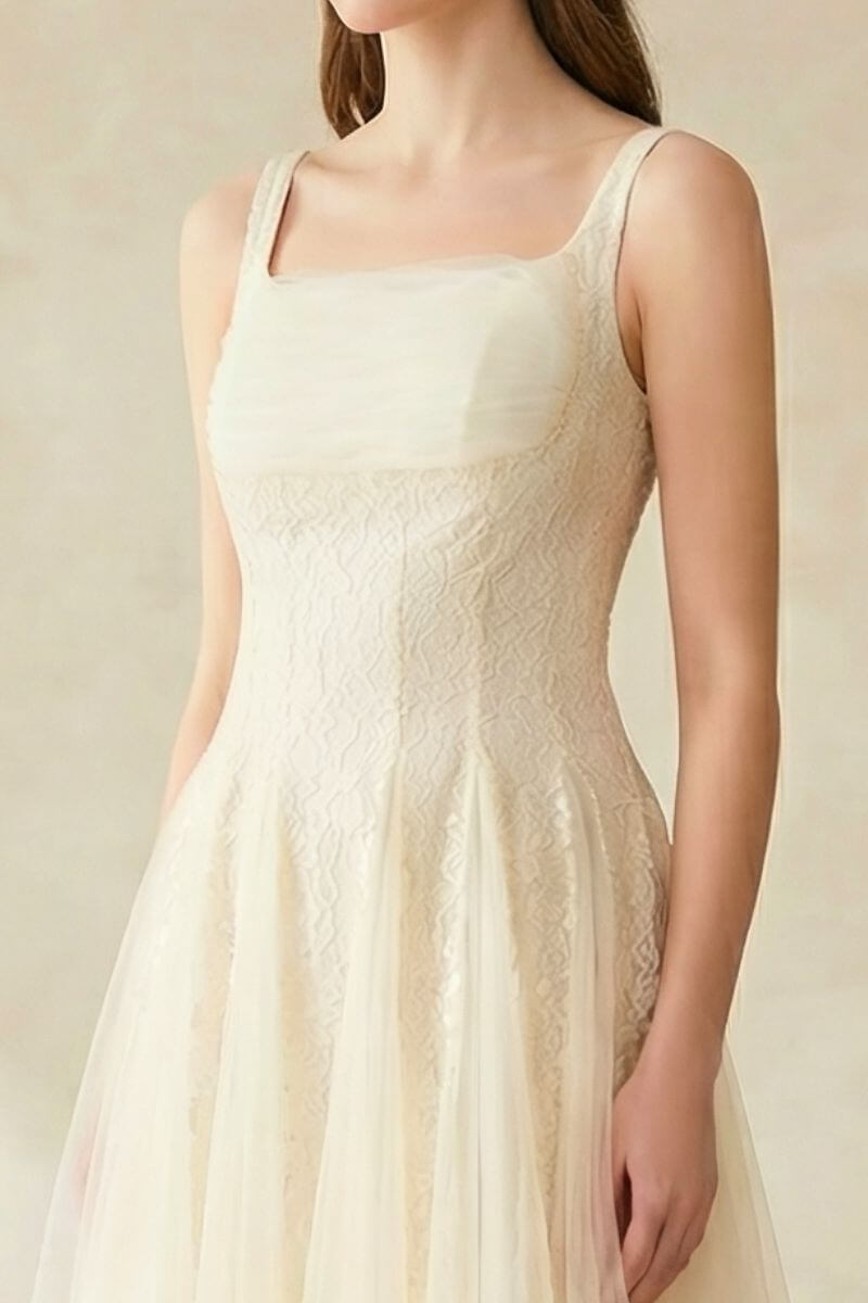 A close-up of the bodice of an ivory lace tulle dress showing textured lace details and wide straps.