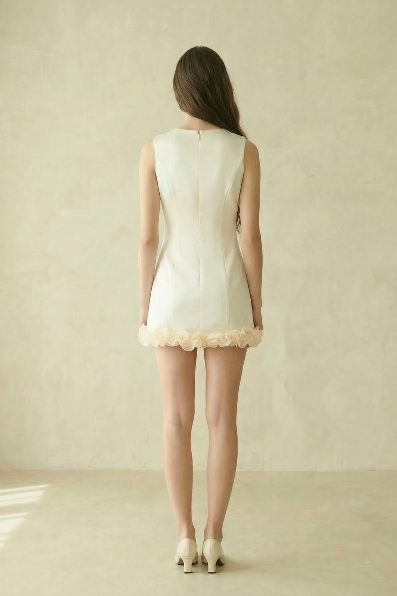 back view of an ivory sleeveless mini dress with concealed zipper and rosette hem, shown in a soft neutral studio setting.