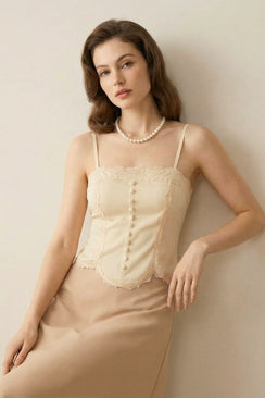 Model leaning gently while wearing an ivory lace-trim corset top and beige midi skirt, accessorized with pearls in a soft minimalist setting.