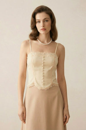 Close-up of an ivory satin corset top with lace trim and covered buttons, styled with a pearl necklace on a model against a soft neutral background.