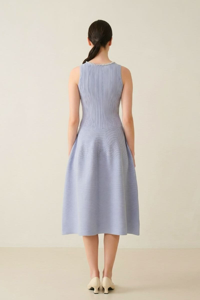 Back view of a light blue sleeveless midi dress featuring a ribbed fitted bodice and a softly structured flared skirt in a minimal studio.