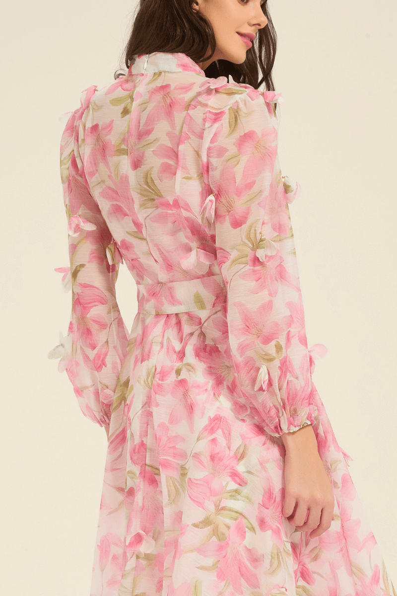 Close-up of pink floral maxi dress highlighting sheer sleeves, petal-like fabric details, and waist tie.