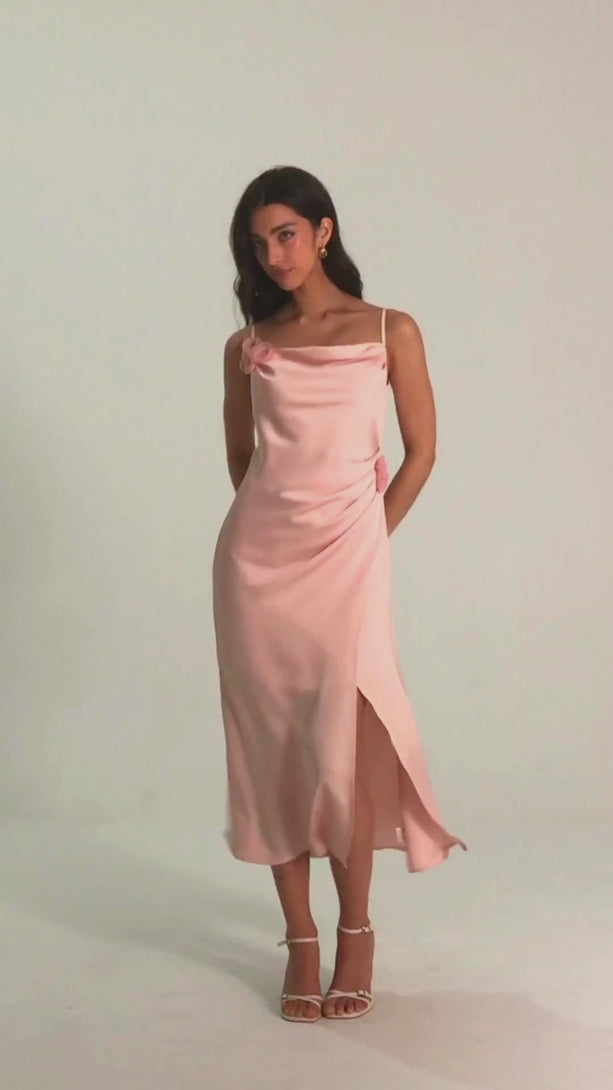 Woman wearing a pink satin slip midi dress with floral rosette details, side slit, and spaghetti straps – front view