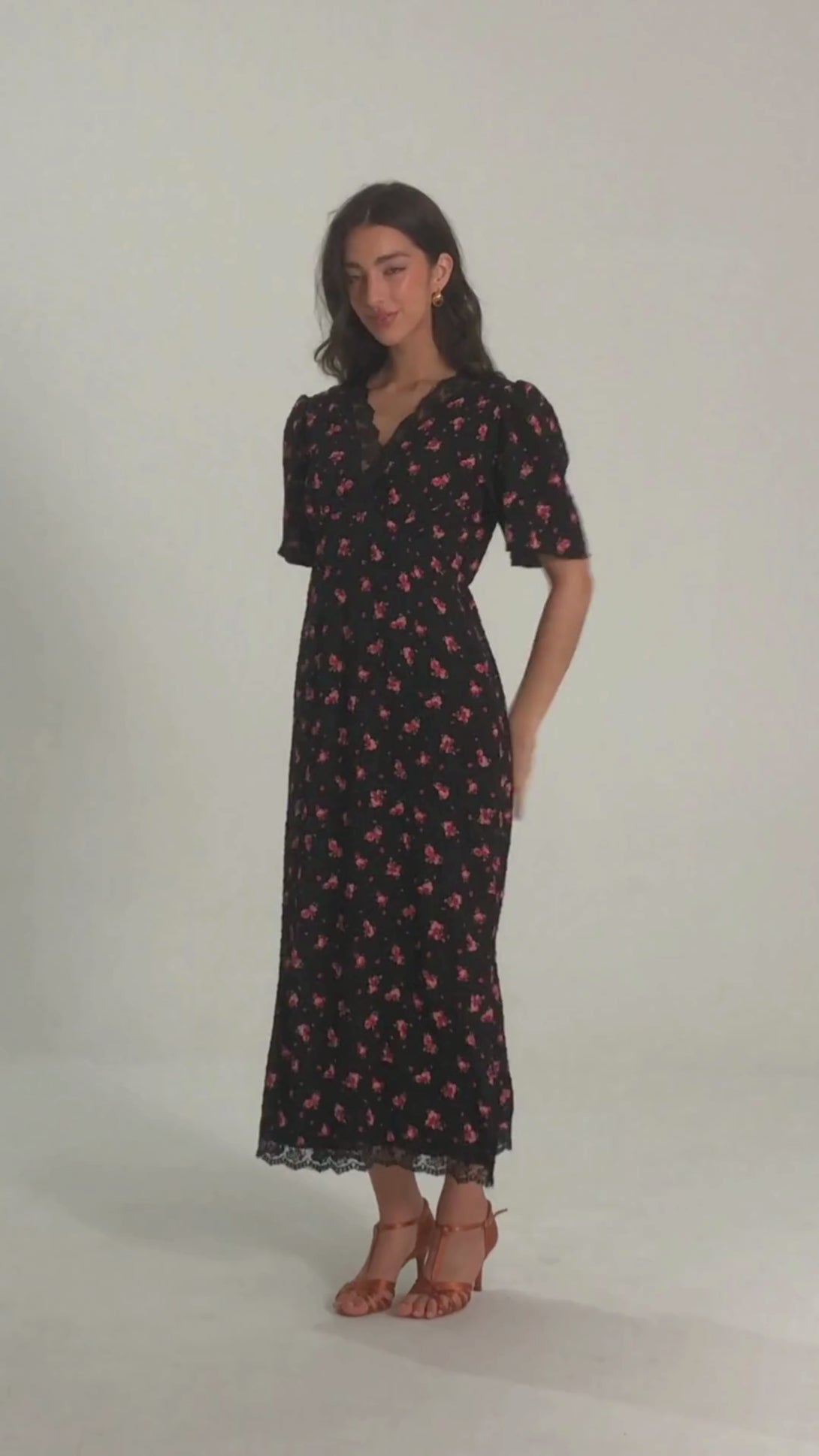 Front view of a woman wearing a black midi dress with red floral print, V-neckline, puff sleeves, and delicate lace trim at the neckline and hem.
