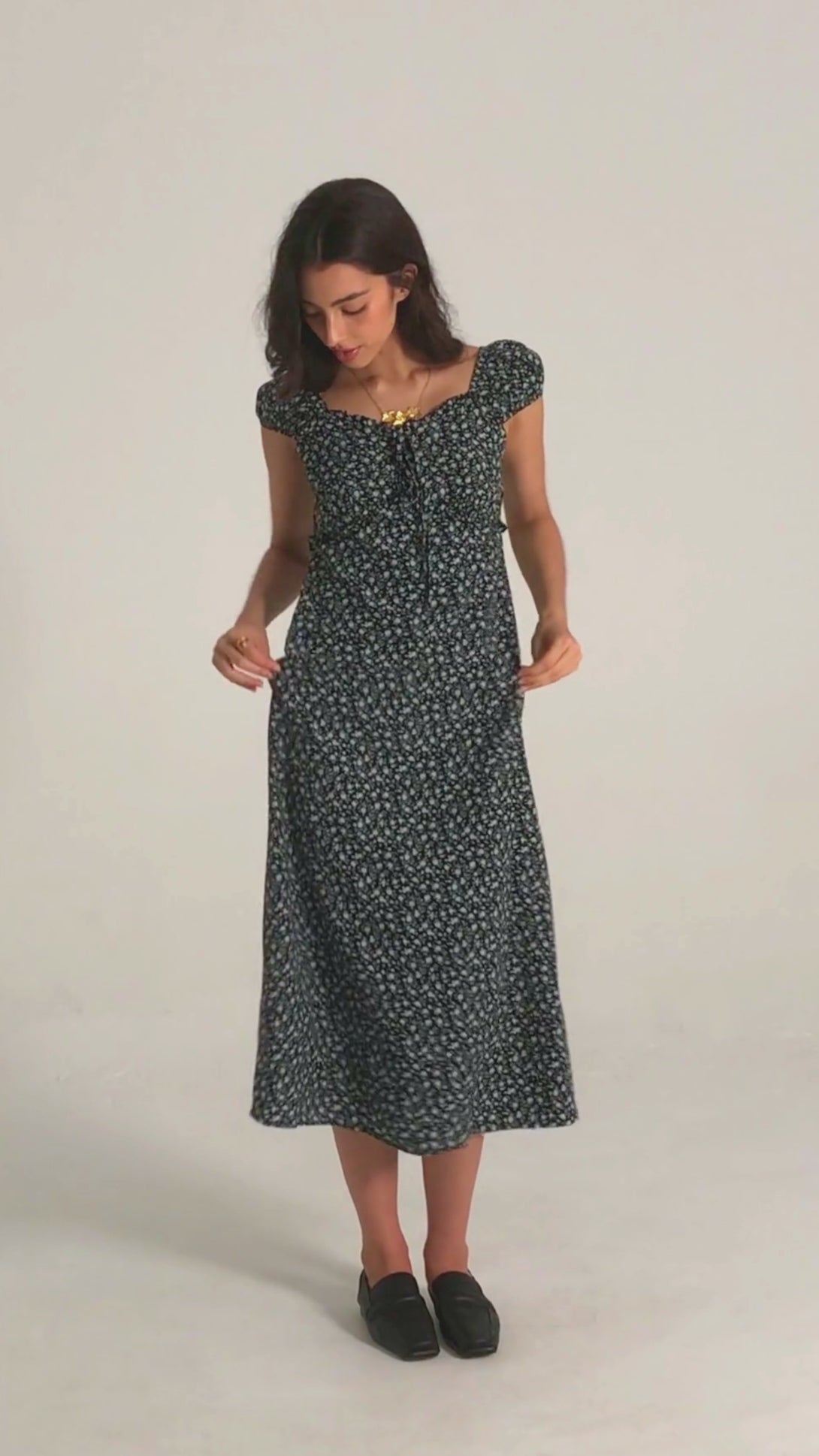 Front view of a woman wearing a black floral midi dress with puff sleeves, ruched bust, and sweetheart neckline